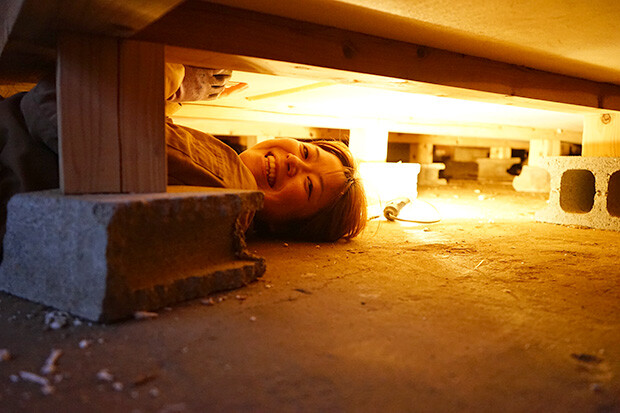床下に潜り込んで笑顔で作業をする女性
