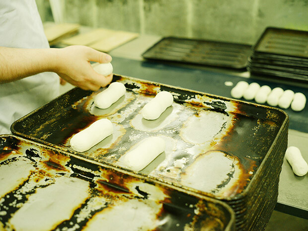 成形した生地を鉄板にのせるのは手作業。コッペパン型に焼けた鉄板が歴史を物語る。発酵する前の小さな生地を見ると、大きなパンをペロリと食べてしまっても許されそうだ。