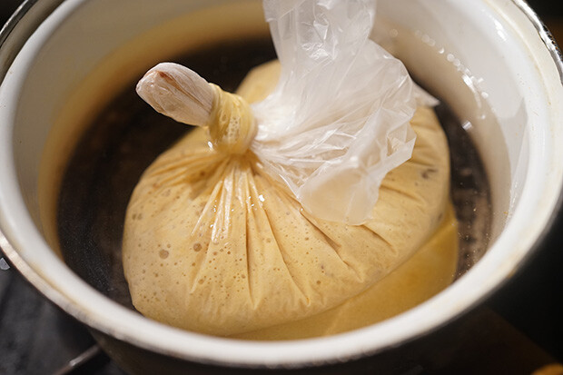 耐熱ポリ袋に蒸しパンの種を入れて口を縛り、湯煎にかけている写真。