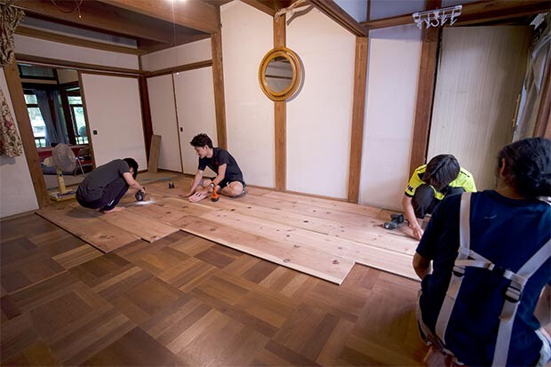 畳の和室の床に木材を敷き、ねじを打ち付けている風景