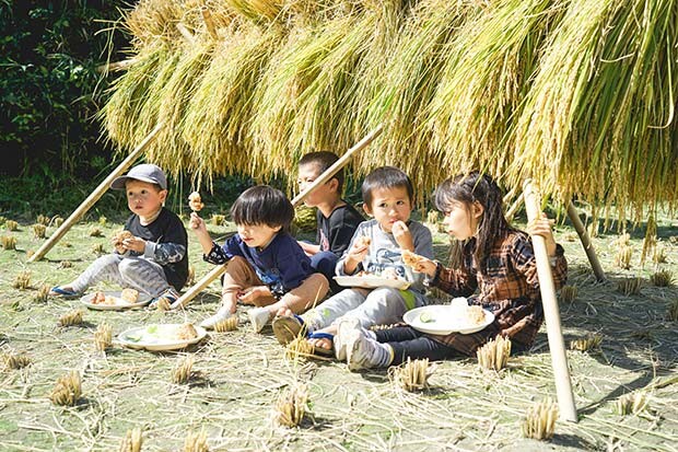 稲刈りの休憩中におにぎりを食べる子どもたち